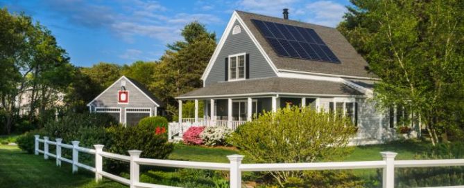 Charming house with solar panels on the roof and a white fence in the foreground