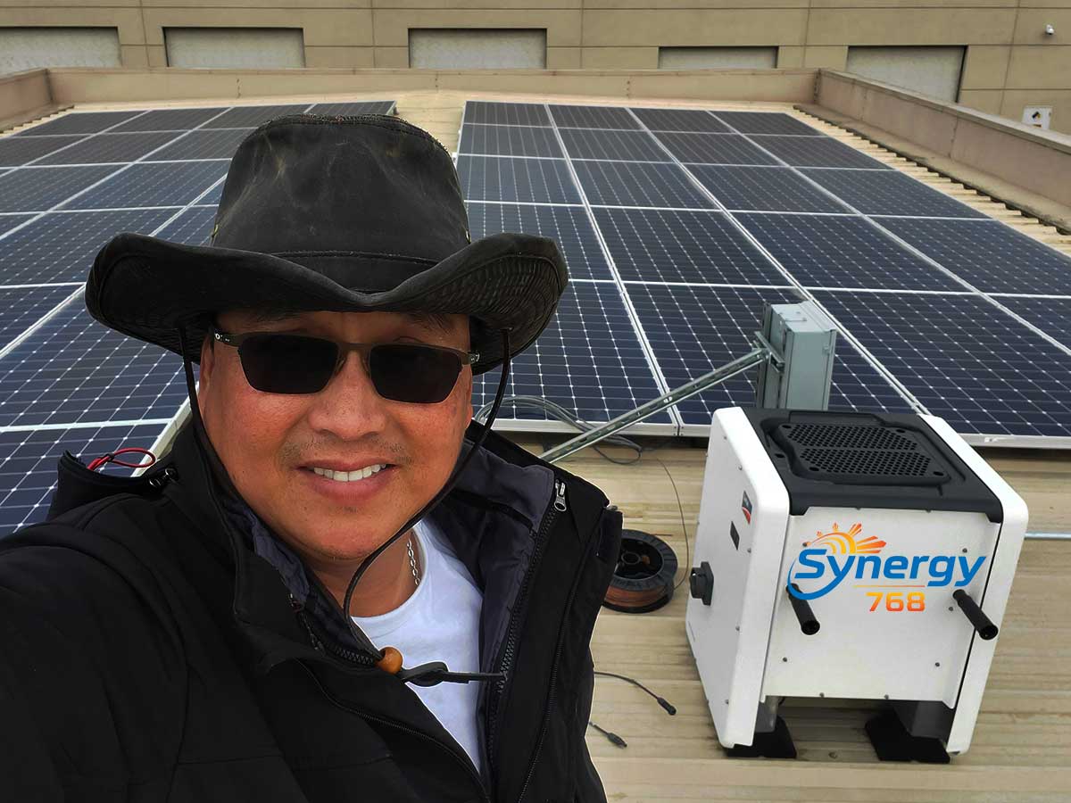 Ed Cotas, owner of Synergy 768, showcasing a rooftop solar panel installation alongside Synergy 768 equipment.